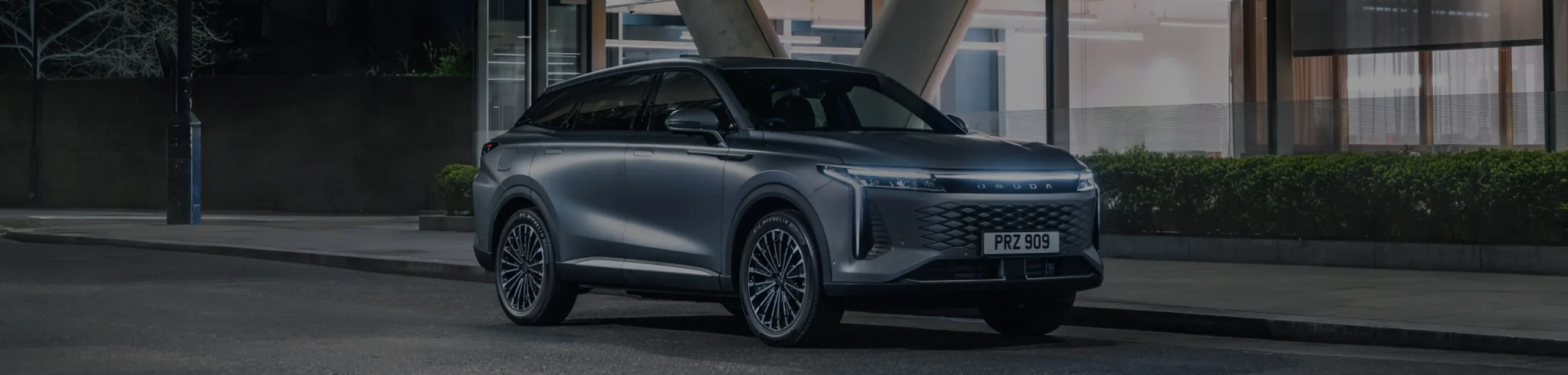 OMODA SUV parked outside a glass building on a road