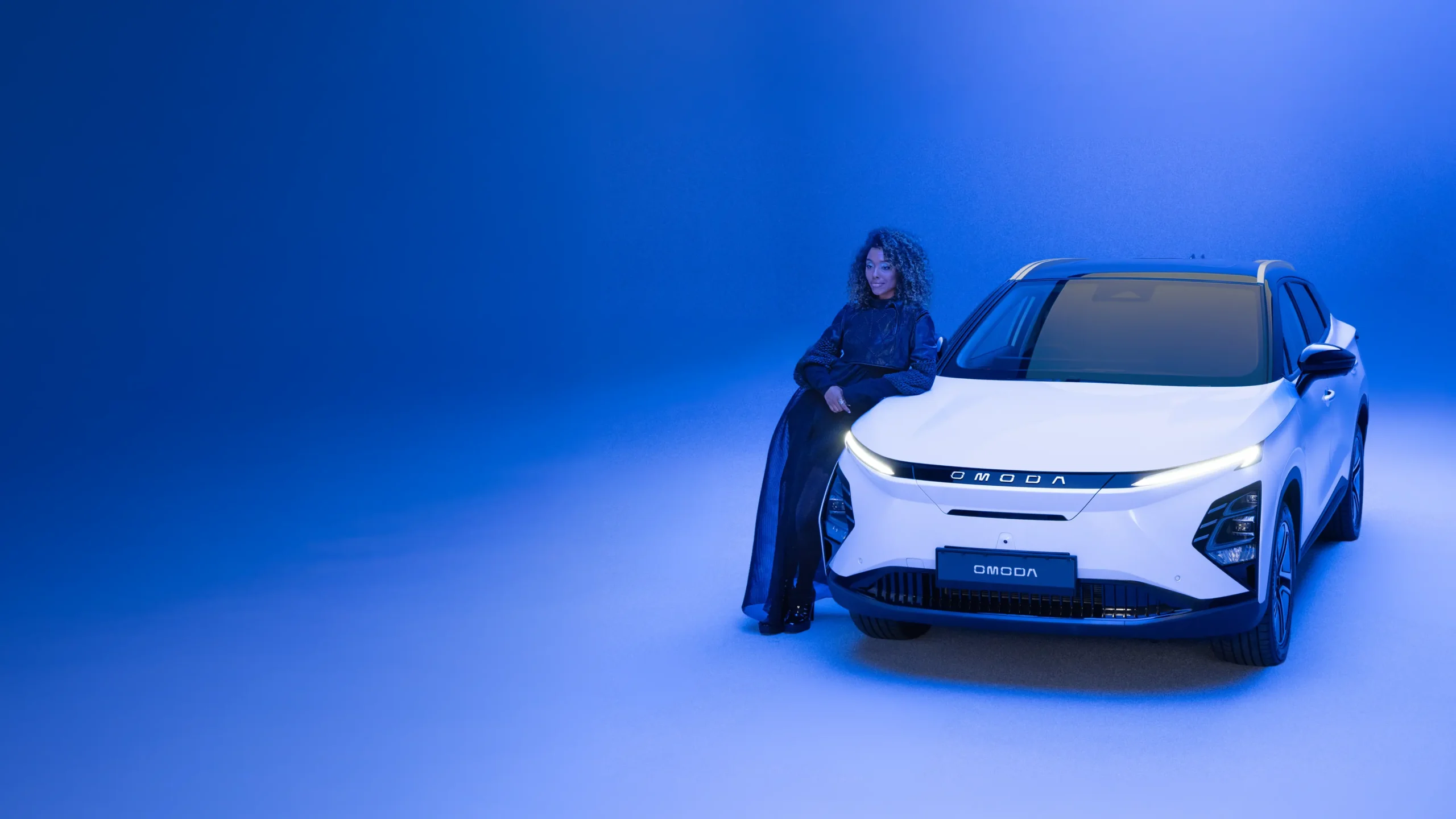 Woman dressed in black leaning on white OMODA in a blue environment