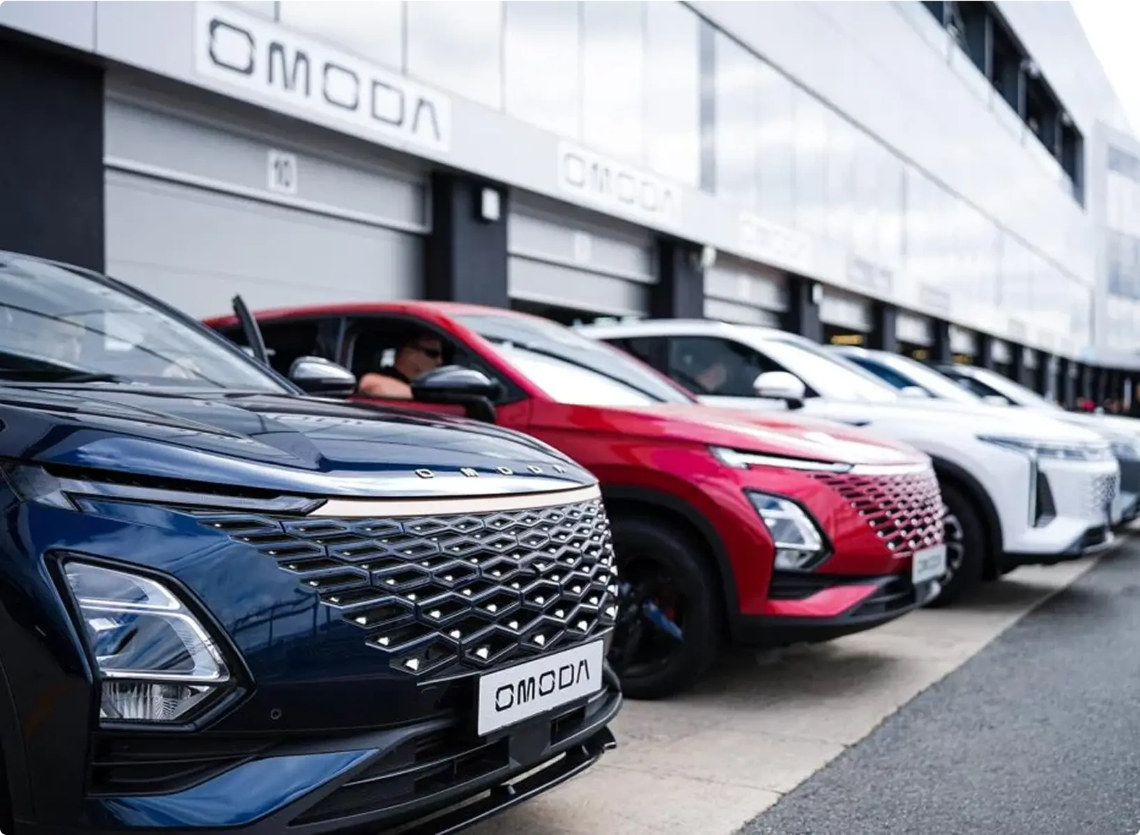 Close up of OMODAs parked in front of dealership. Cars are blue, red and white